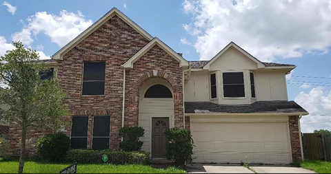 A brick house with a garage door and a tree in front.