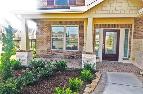 a front porch of a brick house with a walkway and plants