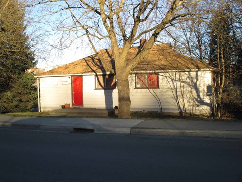 a small white house with a red door and a tree