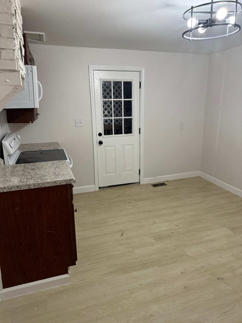 an empty room with a white door and a kitchen