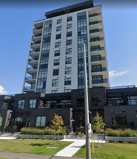 A modern multi-story building with a glass facade and a mix of white and dark grey balconies.
