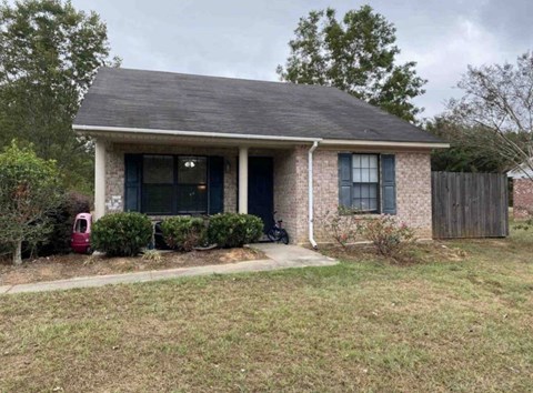 a small brick house with a porch and a black fence