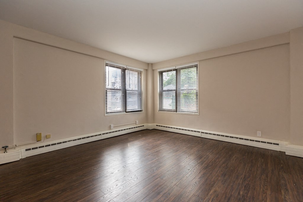 the living room of an empty house with wood flooring and two windows