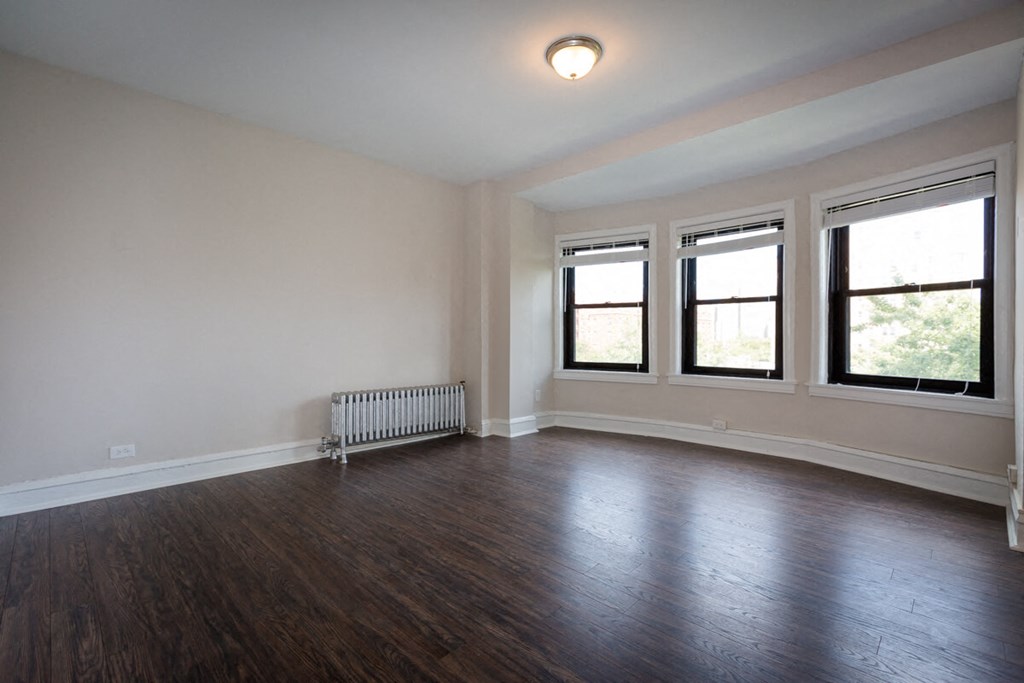an empty living room with wood flooring and three windows