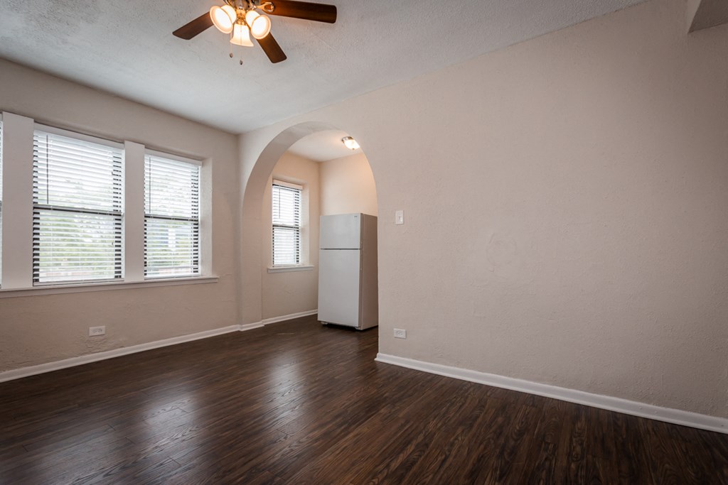 the living room of an empty house with a refrigerator and a ceiling fan