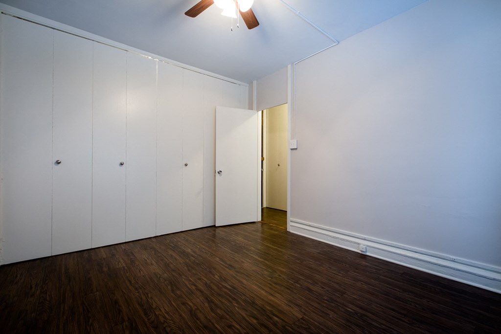 a bedroom with white walls and wood floors and a ceiling fan