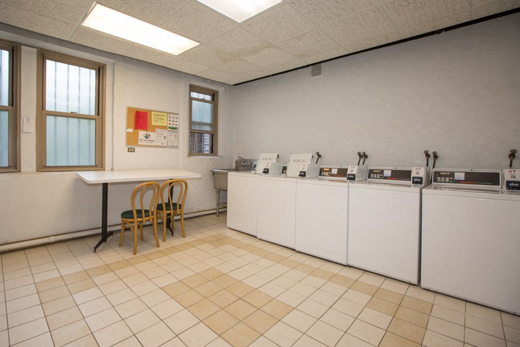 a laundry room with white machines and a table with two yellow chairs
