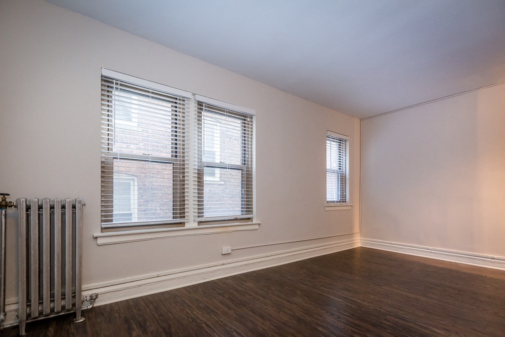 an empty living room with a radiator and two windows