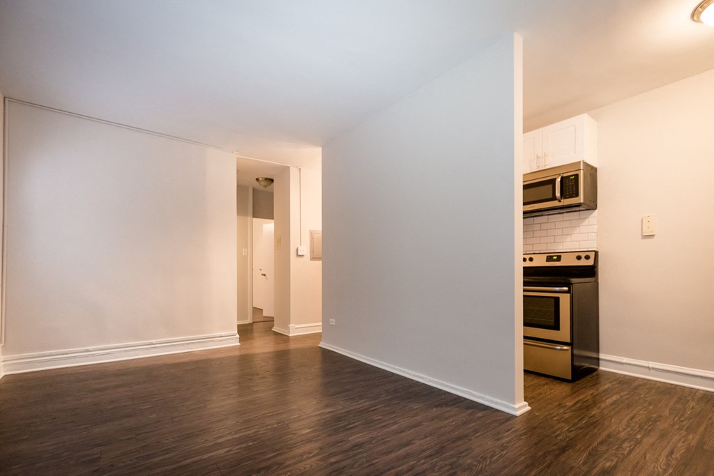 a living room with white walls and a kitchen with stainless steel appliances and wood floors