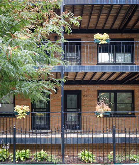 the front of a brick building with a fence and plants
