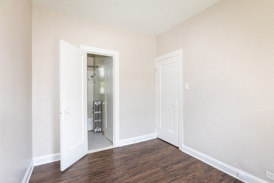 a bedroom with white walls and wood flooring and a closet