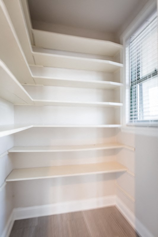 a walk in closet with white shelves and a window