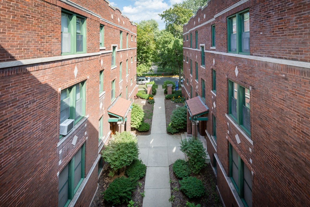 a courtyard between two red brick buildings with trees and bushes