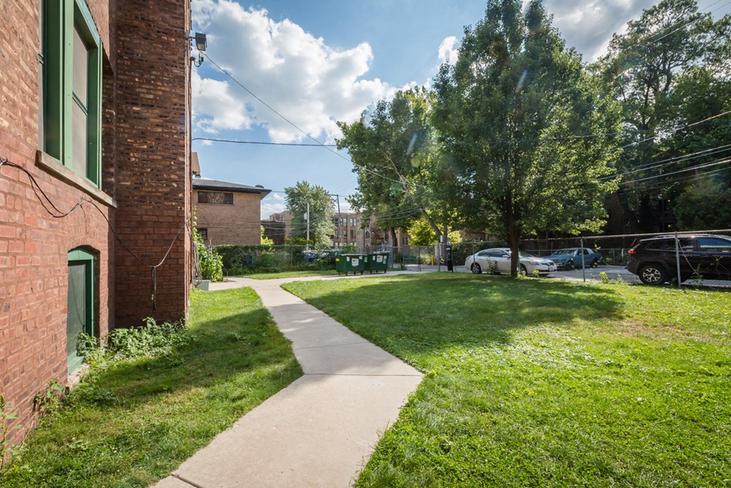 a sidewalk in front of a brick building with grass and trees