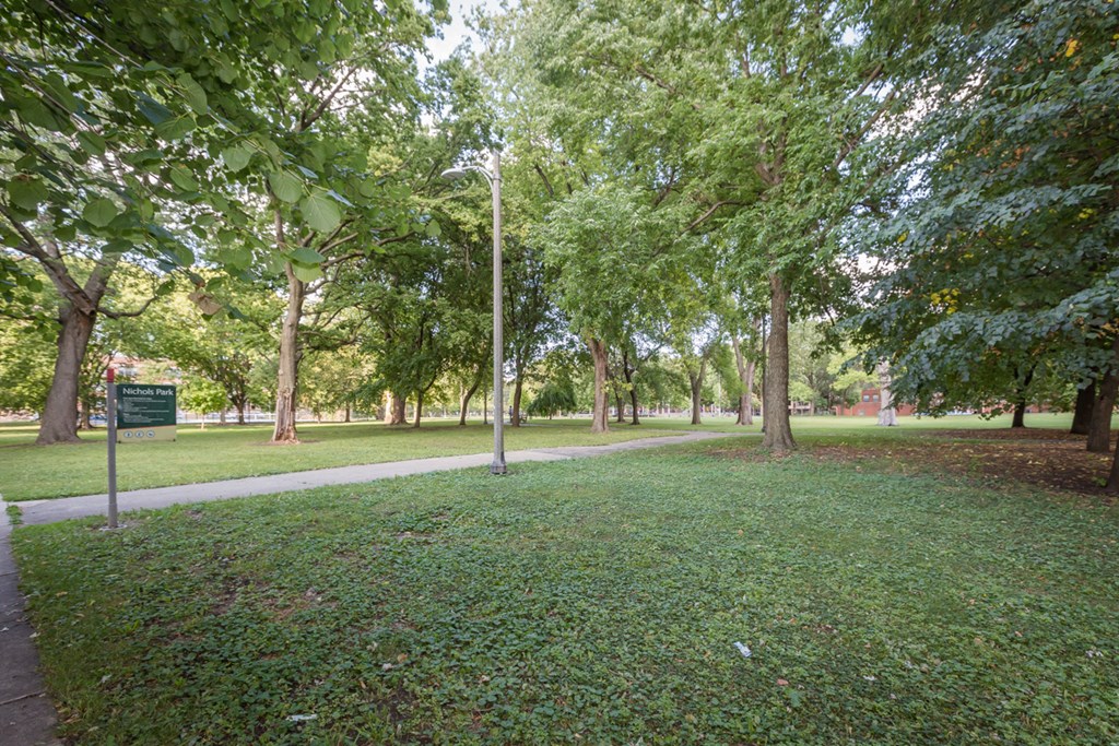 a park with green grass and trees and a sidewalk