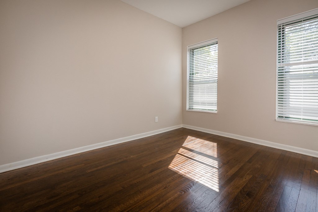 an empty room with wooden floors and two windows