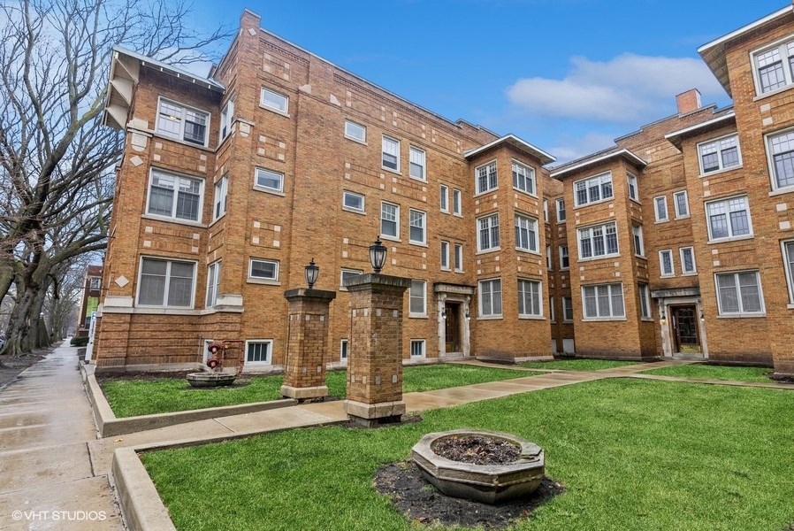 a large brick apartment building with green grass and a fountain