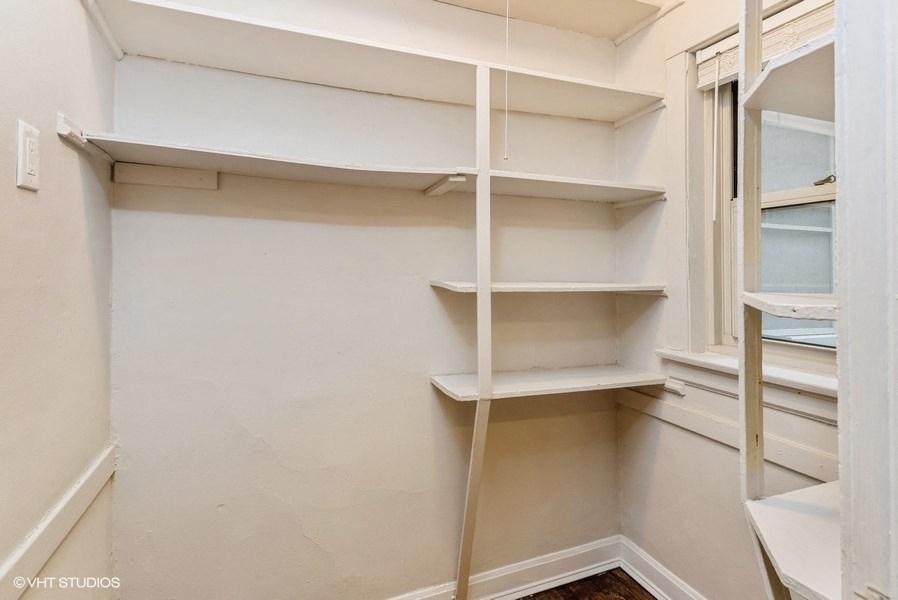 a walk in closet with white shelves and a window