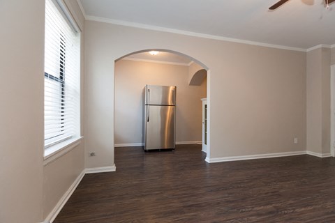 an empty living room with a large window and a stainless steel refrigerator