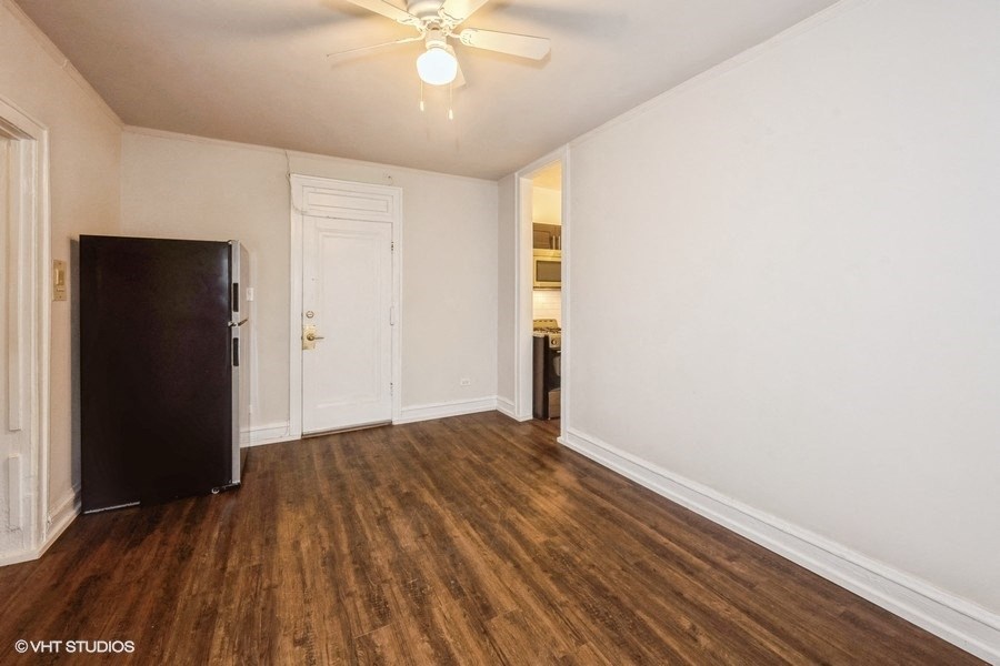an empty living room with a refrigerator and a ceiling fan