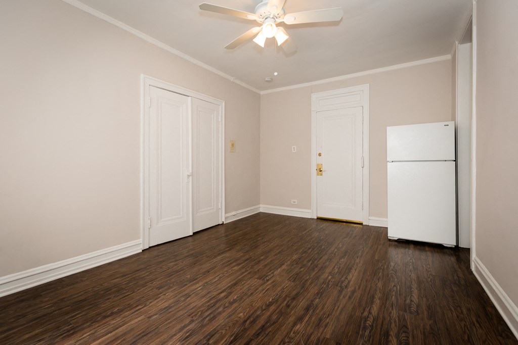 an empty living room with a refrigerator and a ceiling fan