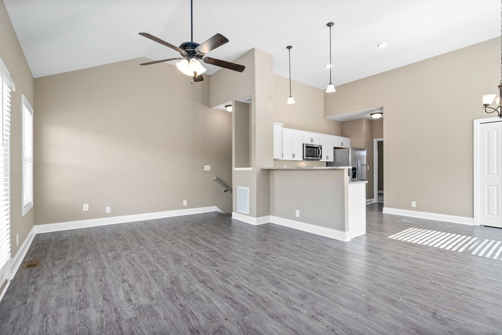 an empty living room with a ceiling fan and a kitchen