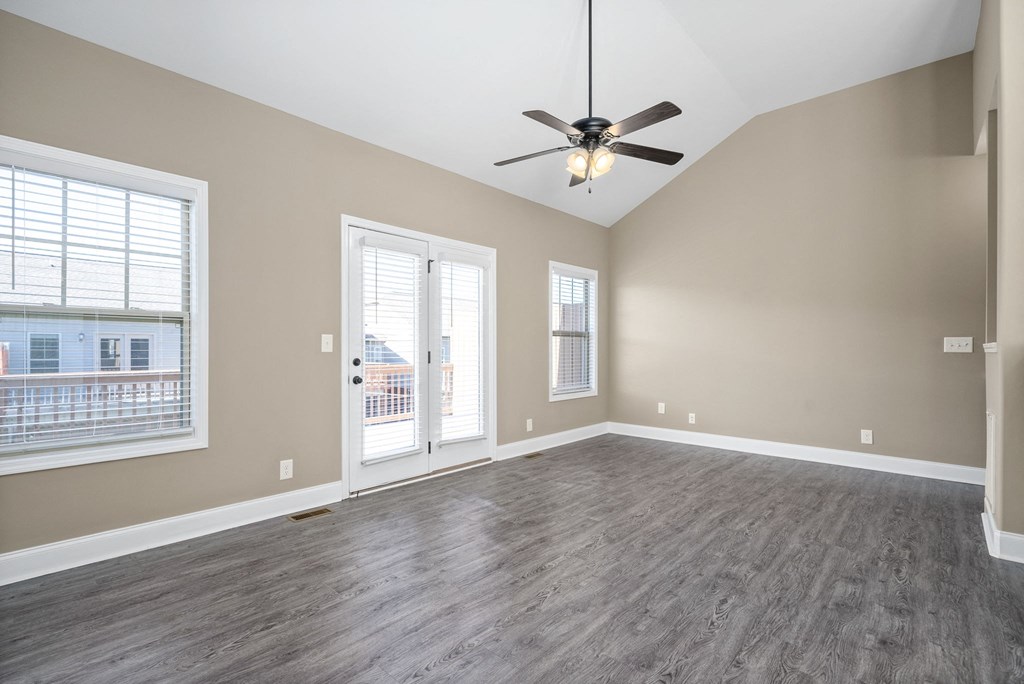 an empty living room with a ceiling fan and windows
