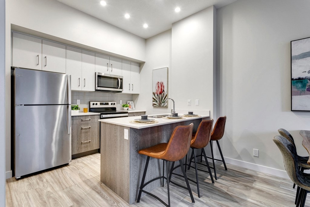 a kitchen with stainless steel appliances and a counter with three chairs
