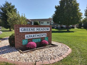 a sign for green meadow apartments in front of a yard with grass and trees