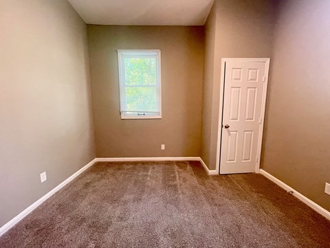 A room with a carpeted floor, a door, and a window.