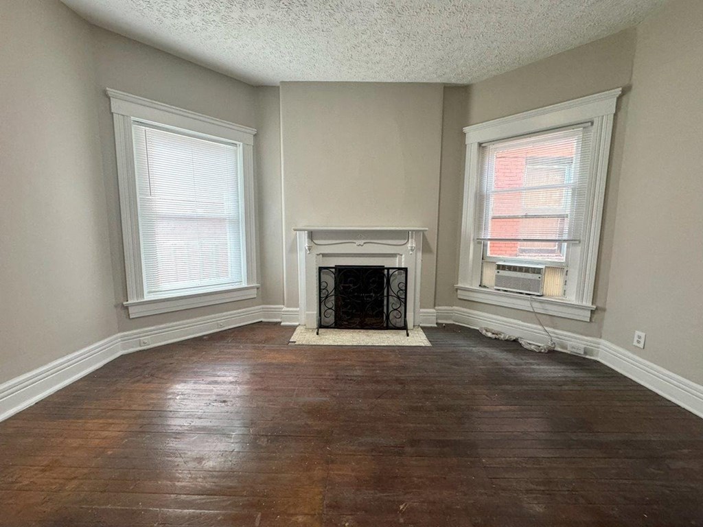 an empty living room with a fireplace and two windows