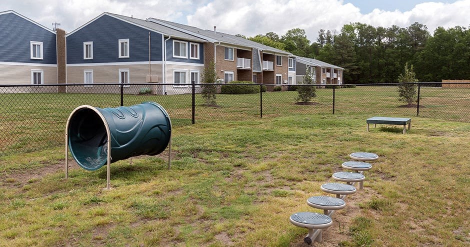 fenced in dog park with grass and agility equipment