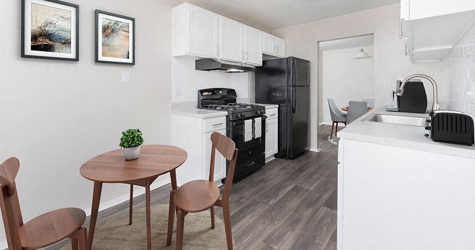 apartment kitchen with white cabinets, black appliances, gray plank flooring and a small table