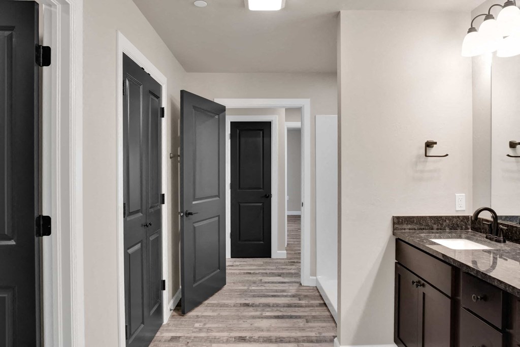 a bathroom with dark doors and a sink and a hallway with closets