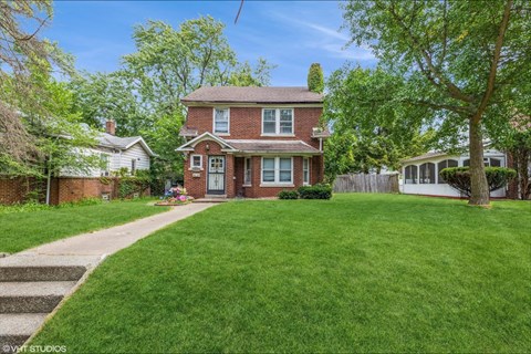 a red brick house with a lawn and a sidewalk