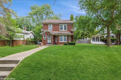 a red brick house with a lawn and a sidewalk