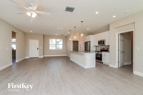 an empty living room with a kitchen and a ceiling fan