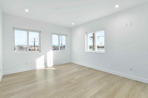 A spacious room with wooden flooring and three windows.