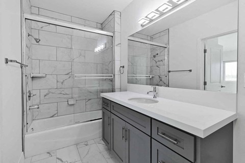 A bathroom with a marble tile shower and a white countertop.