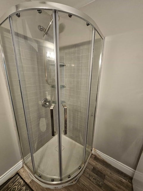 A shower stall with a glass door and a brown floor.