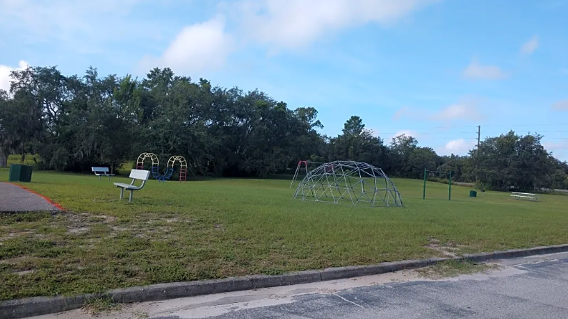 A playground with a swing set and a green trash can.
