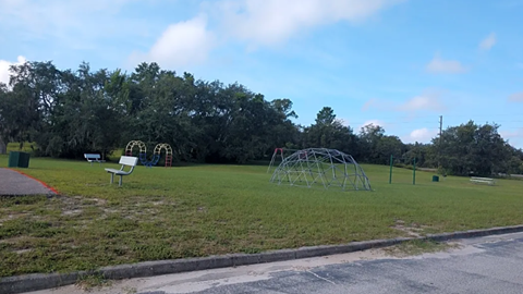 A playground with a swing set and a green trash can.