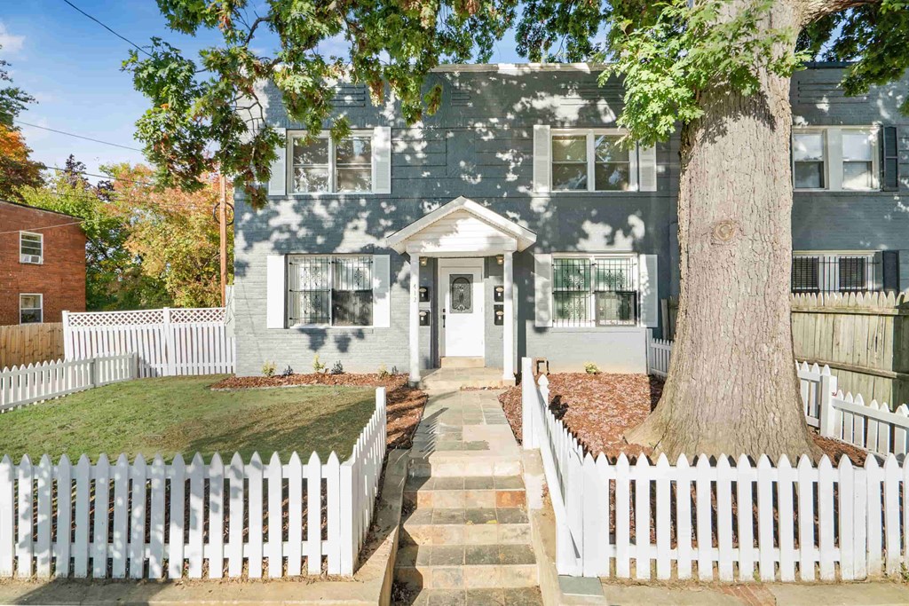 a blue house with a white picket fence and a large tree