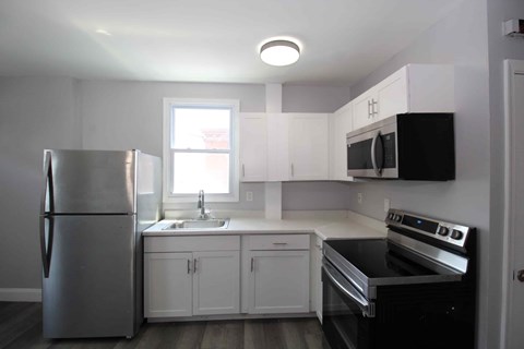 A kitchen with a stainless steel refrigerator, black stove, and white cabinets.