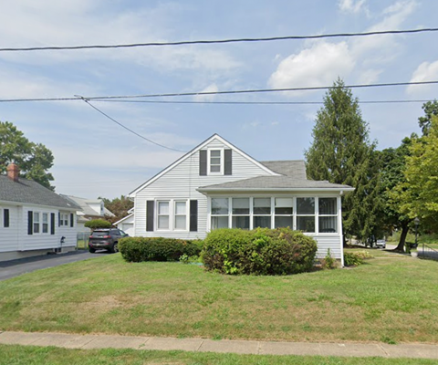 A house with a white exterior and a grey roof is surrounded by greenery.