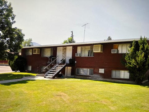 a red brick apartment building with a green yard and a staircase