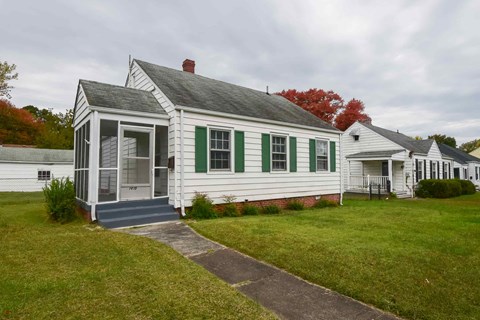 a white house with green shutters and a sidewalk in front of it