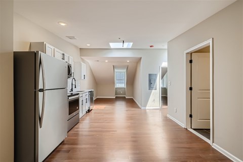 A kitchen with a refrigerator on the left and a hallway leading to a bathroom.