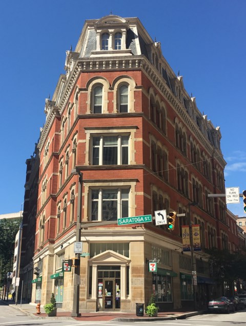 A tall red brick building with a green awning on the corner of a street.