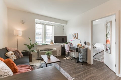 A living room with a couch, a coffee table, and a bedroom with a bed and a desk.